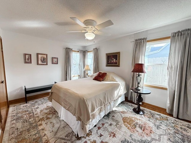 bedroom featuring ceiling fan, baseboards, a textured ceiling, and wood finished floors