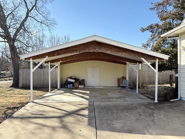 view of parking / parking lot featuring a carport, concrete driveway, and fence