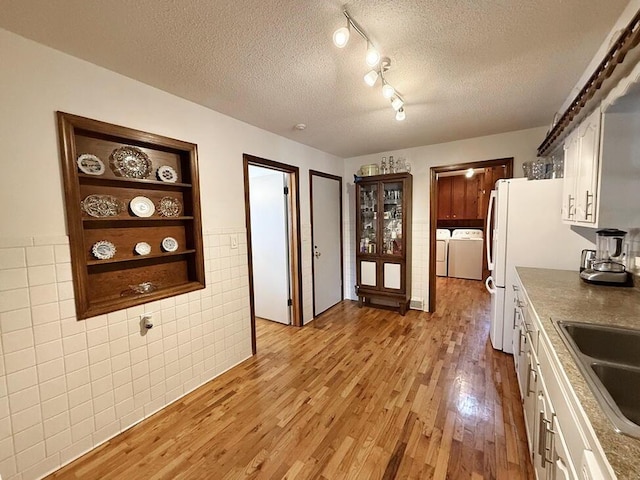 kitchen with light wood-style floors, white cabinets, a textured ceiling, and washing machine and clothes dryer