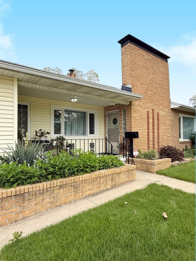view of front of house with covered porch, brick siding, a chimney, and a front lawn