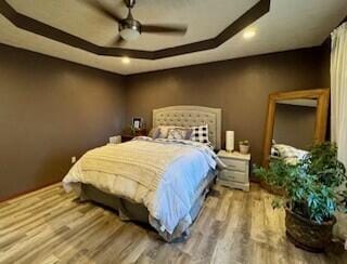 bedroom with ceiling fan, wood finished floors, and a raised ceiling