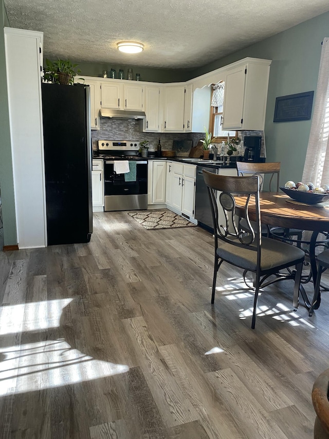 kitchen with white cabinets, dark countertops, wood finished floors, stainless steel appliances, and under cabinet range hood