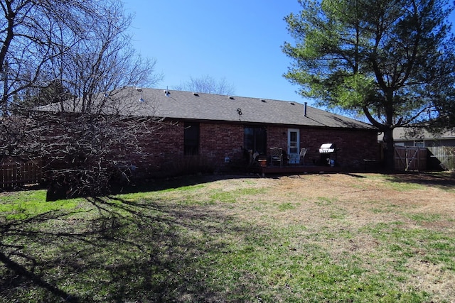 rear view of house featuring brick siding, roof with shingles, a deck, and a yard