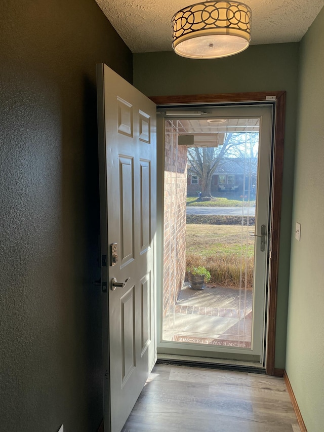 doorway to outside featuring a textured wall, a textured ceiling, and wood finished floors