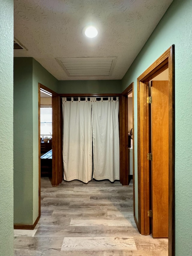 hallway with light wood-style floors, visible vents, a textured wall, and a textured ceiling