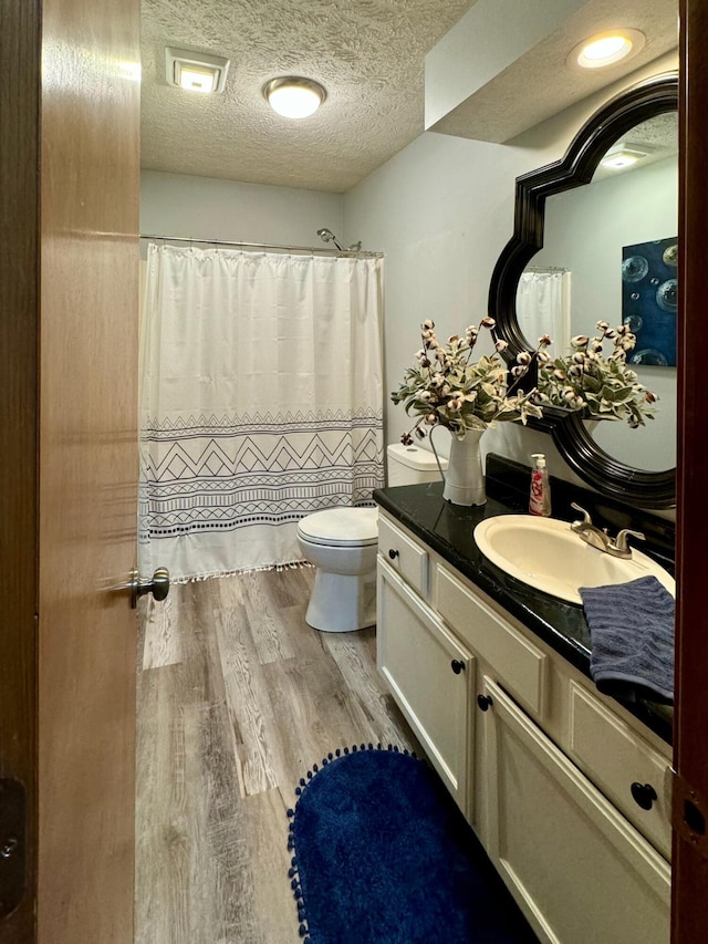 full bath featuring curtained shower, toilet, a textured ceiling, vanity, and wood finished floors