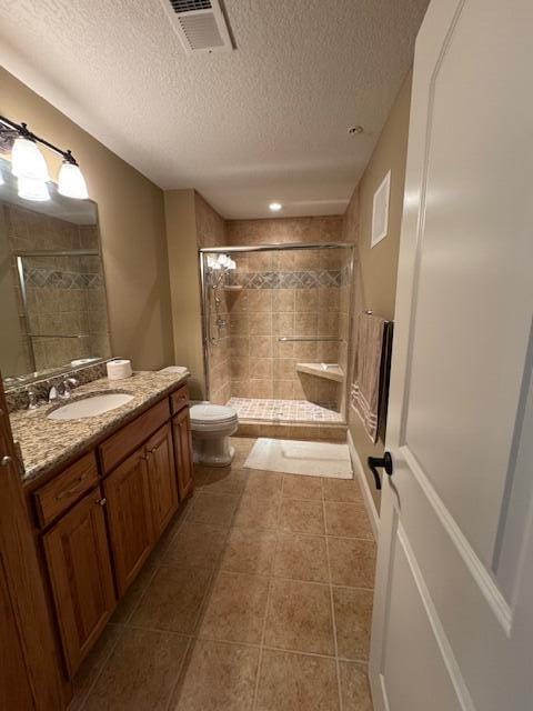 full bath with a textured ceiling, tile patterned flooring, toilet, vanity, and a tile shower