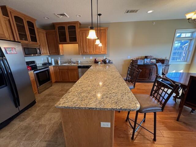 kitchen with appliances with stainless steel finishes, glass insert cabinets, a sink, a peninsula, and a kitchen bar