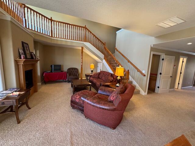 carpeted living room with baseboards, visible vents, stairs, a textured ceiling, and a fireplace