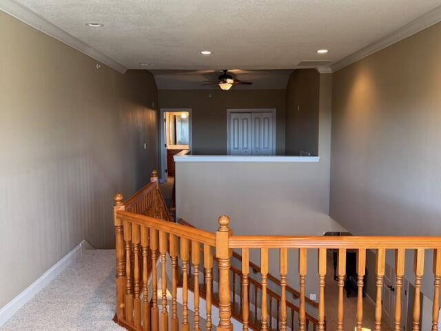 hallway with baseboards, ornamental molding, carpet, a textured ceiling, and an upstairs landing