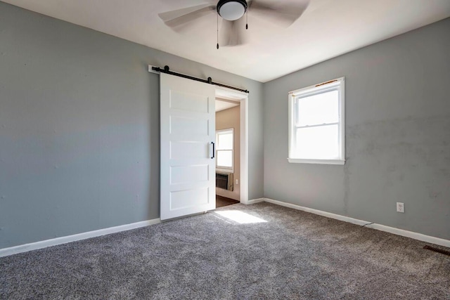 unfurnished bedroom featuring a barn door, visible vents, baseboards, ceiling fan, and carpet floors