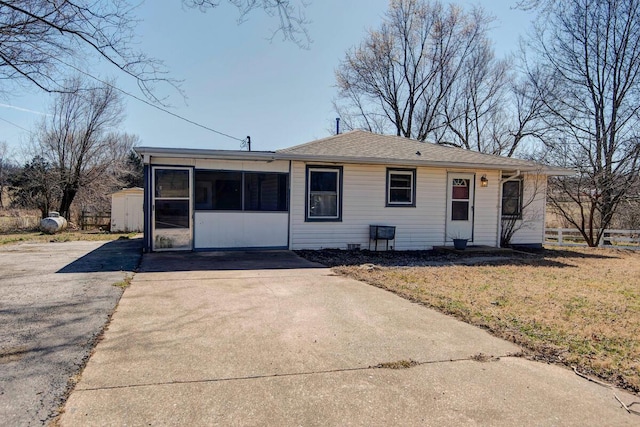 view of front of house featuring a shingled roof, a sunroom, fence, driveway, and a front lawn