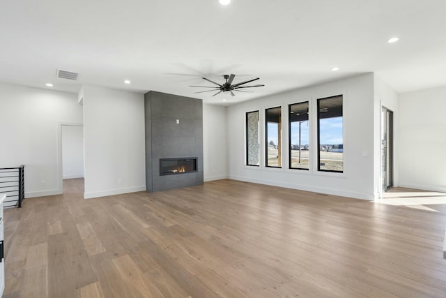 unfurnished living room with a large fireplace, light wood finished floors, baseboards, visible vents, and recessed lighting