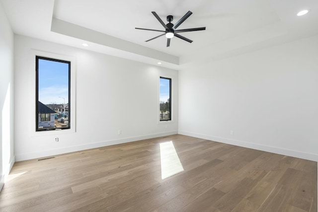 unfurnished room with light wood finished floors, baseboards, a raised ceiling, and recessed lighting