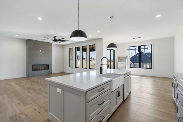 kitchen with light wood-style flooring, a large fireplace, a sink, light countertops, and dishwasher