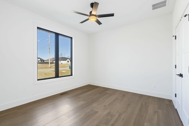 empty room featuring a ceiling fan, wood finished floors, visible vents, and baseboards