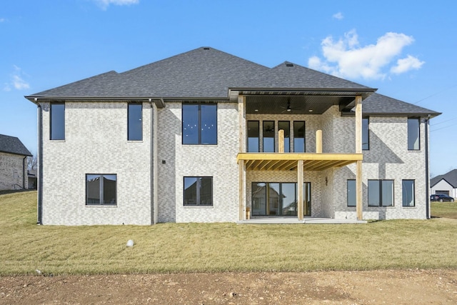 rear view of house featuring a shingled roof, brick siding, a yard, and a balcony