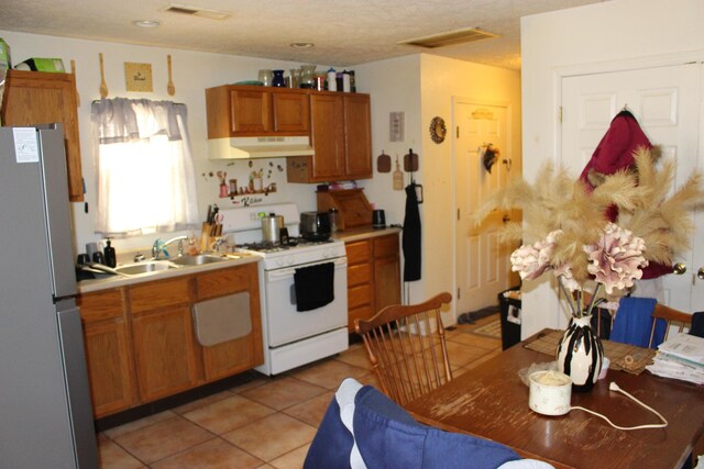 810 W College St, Springfield, MO 65806 - kitchen with gas range gas stove, brown cabinetry, freestanding refrigerator, a sink, and under cabinet range hood