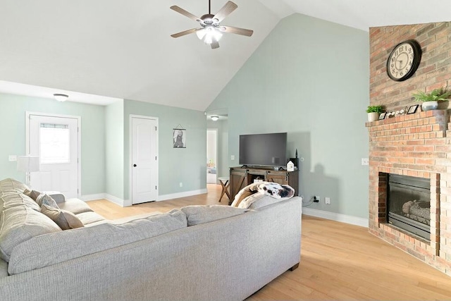 living area with light wood finished floors, baseboards, ceiling fan, a brick fireplace, and high vaulted ceiling