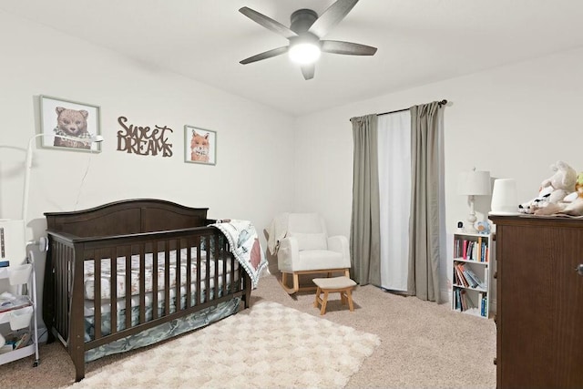 bedroom featuring a nursery area, ceiling fan, and carpet flooring