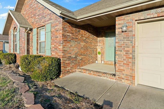 entrance to property with an attached garage, a shingled roof, and brick siding