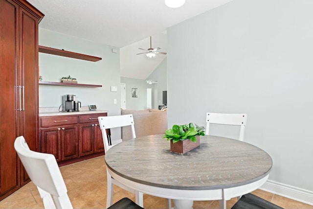 dining space featuring a ceiling fan, vaulted ceiling, baseboards, and light tile patterned floors