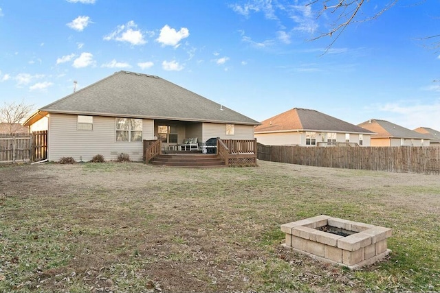 back of property featuring roof with shingles, a yard, an outdoor fire pit, a deck, and a fenced backyard