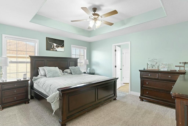 bedroom with light carpet, a tray ceiling, a ceiling fan, and baseboards