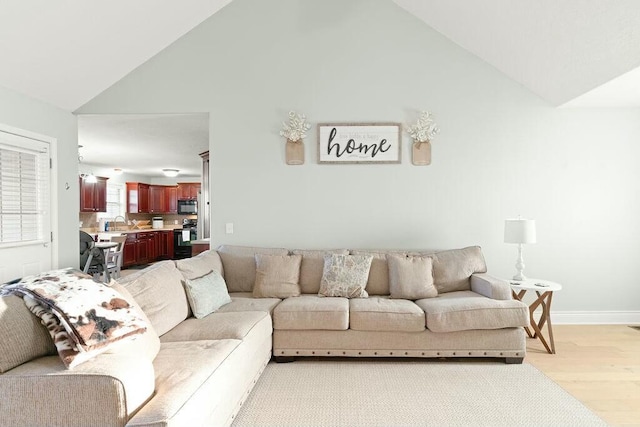 living room featuring high vaulted ceiling, light wood-style flooring, and baseboards