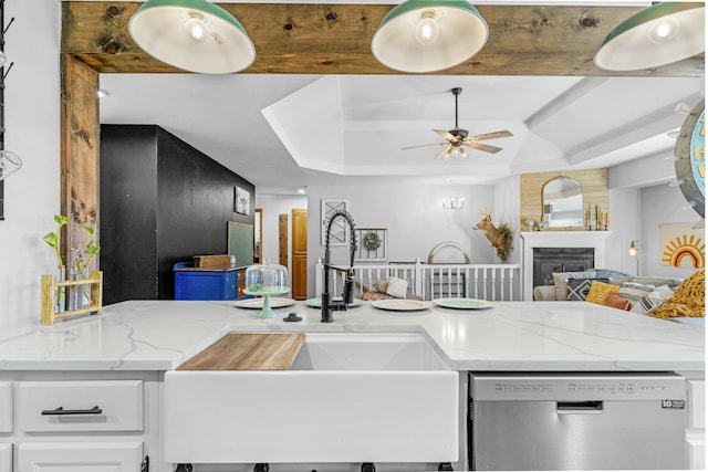 kitchen featuring light stone counters, stainless steel dishwasher, a fireplace, white cabinetry, and a sink