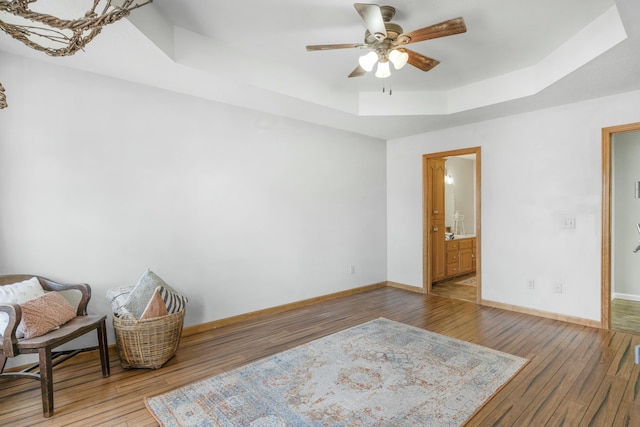 living area with a tray ceiling, baseboards, ceiling fan, and hardwood / wood-style floors