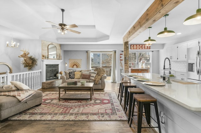 living area featuring a large fireplace, ceiling fan, a tray ceiling, and wood finished floors