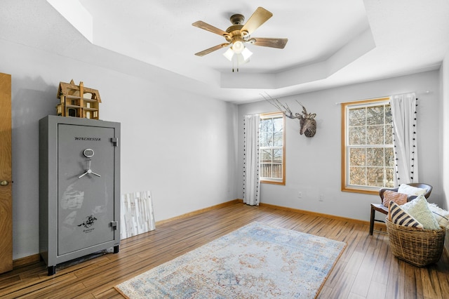 sitting room featuring plenty of natural light, wood-type flooring, a raised ceiling, and baseboards