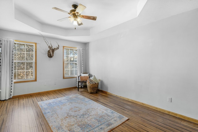 unfurnished room with ceiling fan, hardwood / wood-style floors, a raised ceiling, and baseboards