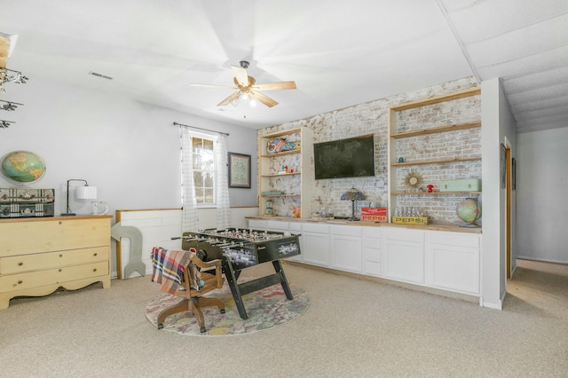 recreation room featuring brick wall, light colored carpet, visible vents, and a ceiling fan