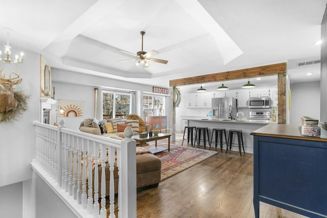 living room featuring visible vents, a raised ceiling, dark wood-type flooring, ceiling fan with notable chandelier, and recessed lighting