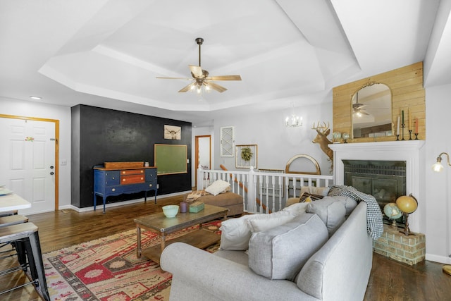 living area featuring baseboards, a raised ceiling, a ceiling fan, a glass covered fireplace, and wood finished floors