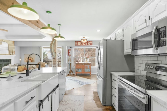 kitchen with stainless steel appliances, wood finished floors, white cabinets, hanging light fixtures, and backsplash