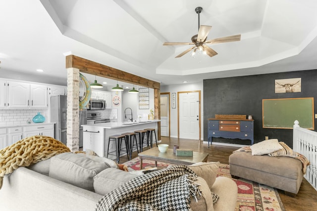 living area featuring a raised ceiling, a ceiling fan, dark wood finished floors, an accent wall, and recessed lighting