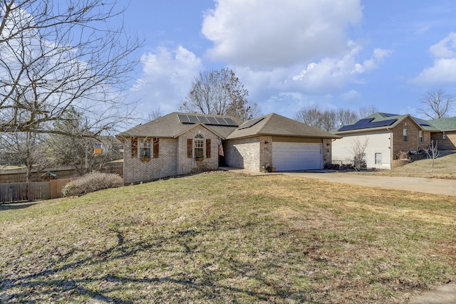 view of front facade featuring brick siding, roof mounted solar panels, fence, driveway, and a front lawn