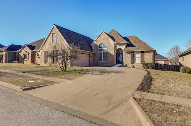 view of front facade with driveway, brick siding, a front yard, and fence