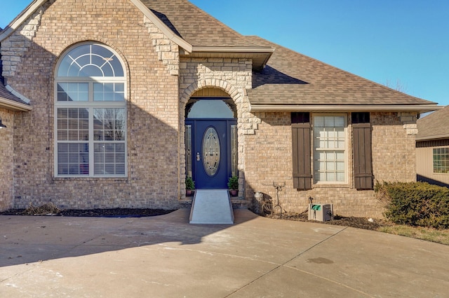 view of exterior entry with brick siding and roof with shingles