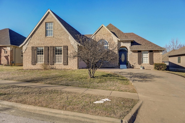 view of front of property with a shingled roof, a front yard, concrete driveway, and brick siding