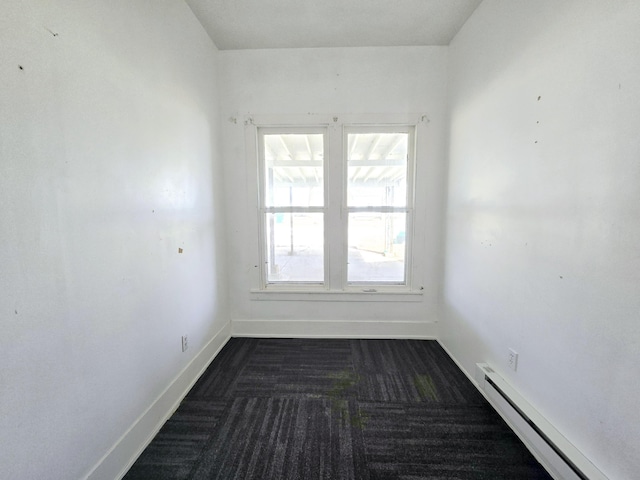 unfurnished room featuring baseboard heating, dark carpet, and baseboards