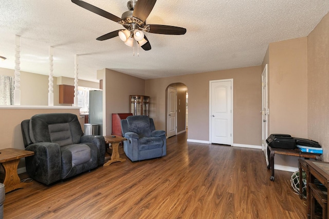 living area with arched walkways, a ceiling fan, a textured ceiling, wood finished floors, and baseboards