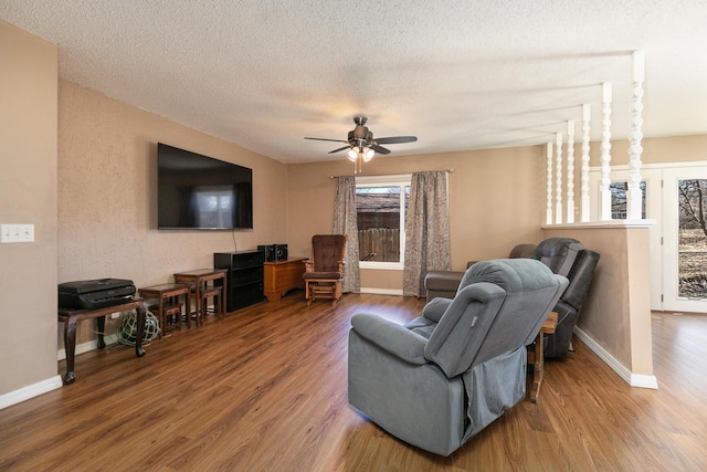 living room with ceiling fan, a textured ceiling, baseboards, and wood finished floors