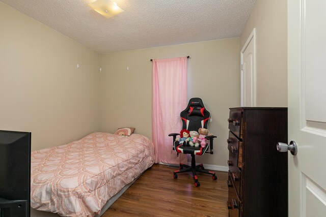 bedroom with a textured ceiling, baseboards, and wood finished floors