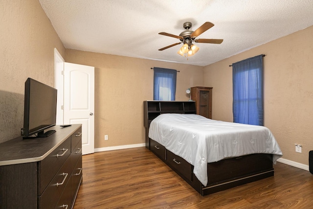 bedroom with a textured wall, dark wood finished floors, baseboards, and ceiling fan