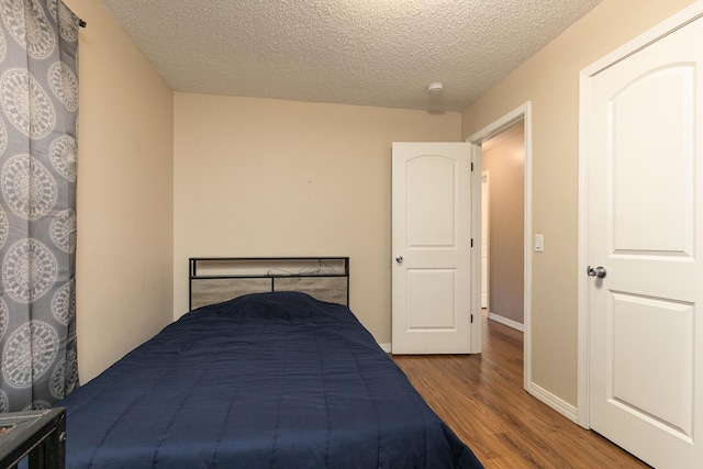 unfurnished bedroom with a textured ceiling, baseboards, and wood finished floors