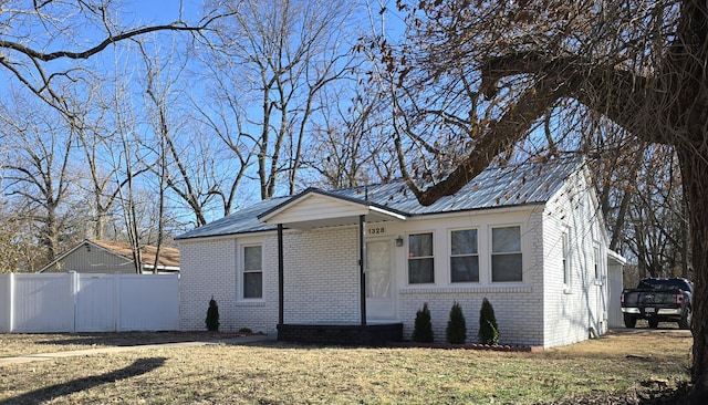 view of front facade featuring a front lawn, fence, metal roof, and brick siding